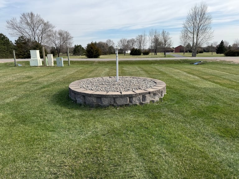 A young tree in the center of a circular stone tree ring filled with gravel on a mowed grass field