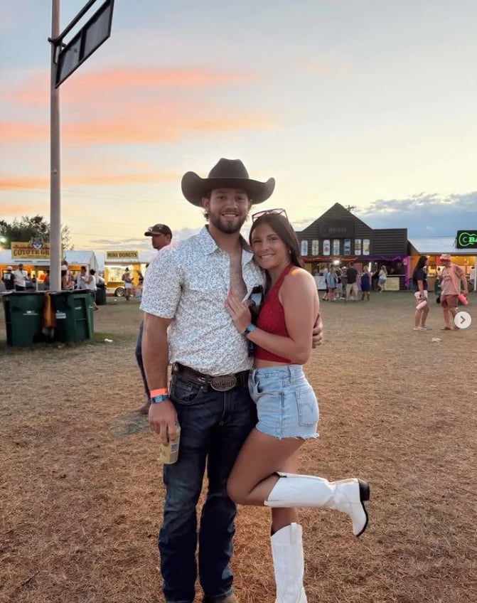 Man in cowboy hat and woman in red top posing together at an outdoor rodeo event at sunset