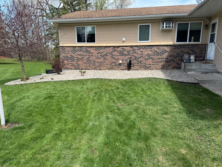 Front exterior of single-story brick and siding home with manicured green lawn and concrete patio