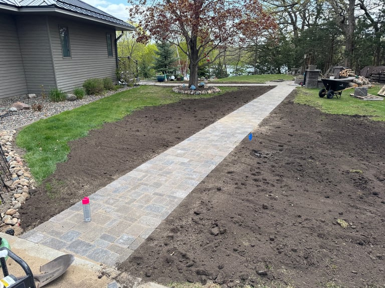 Backyard landscape construction with newly laid paver walkway through freshly tilled soil bed beside a house