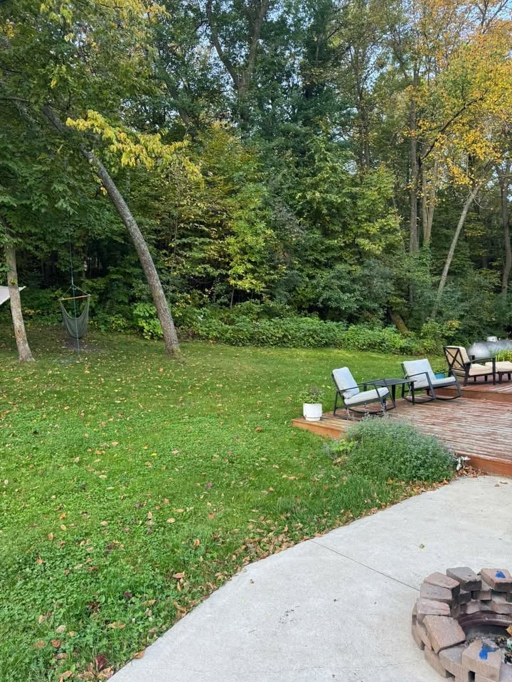Backyard patio area with lounge chairs on wooden deck, manicured lawn, and surrounding forest trees during early autumn